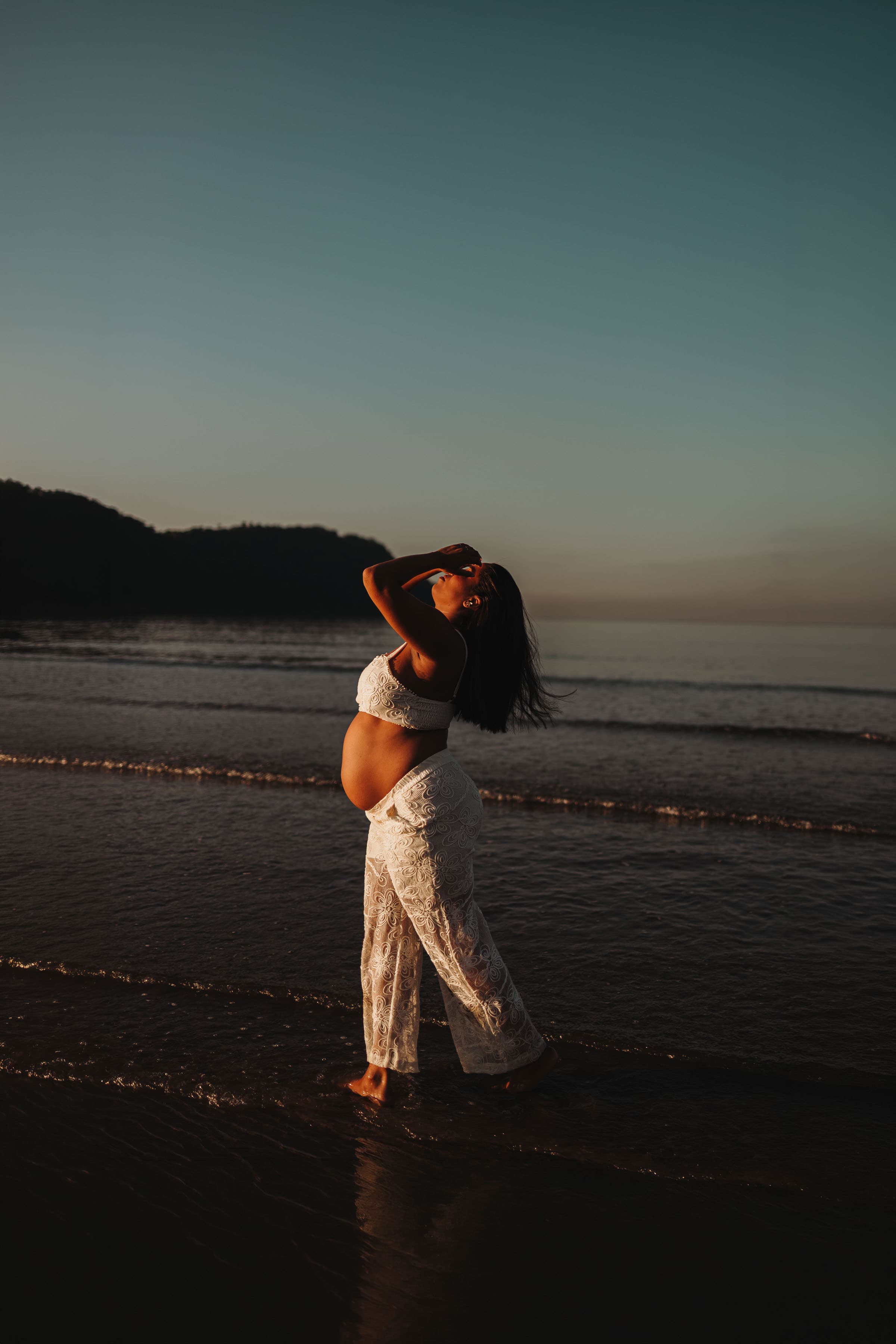 Gestante na praia ao entardecer, vestido de renda