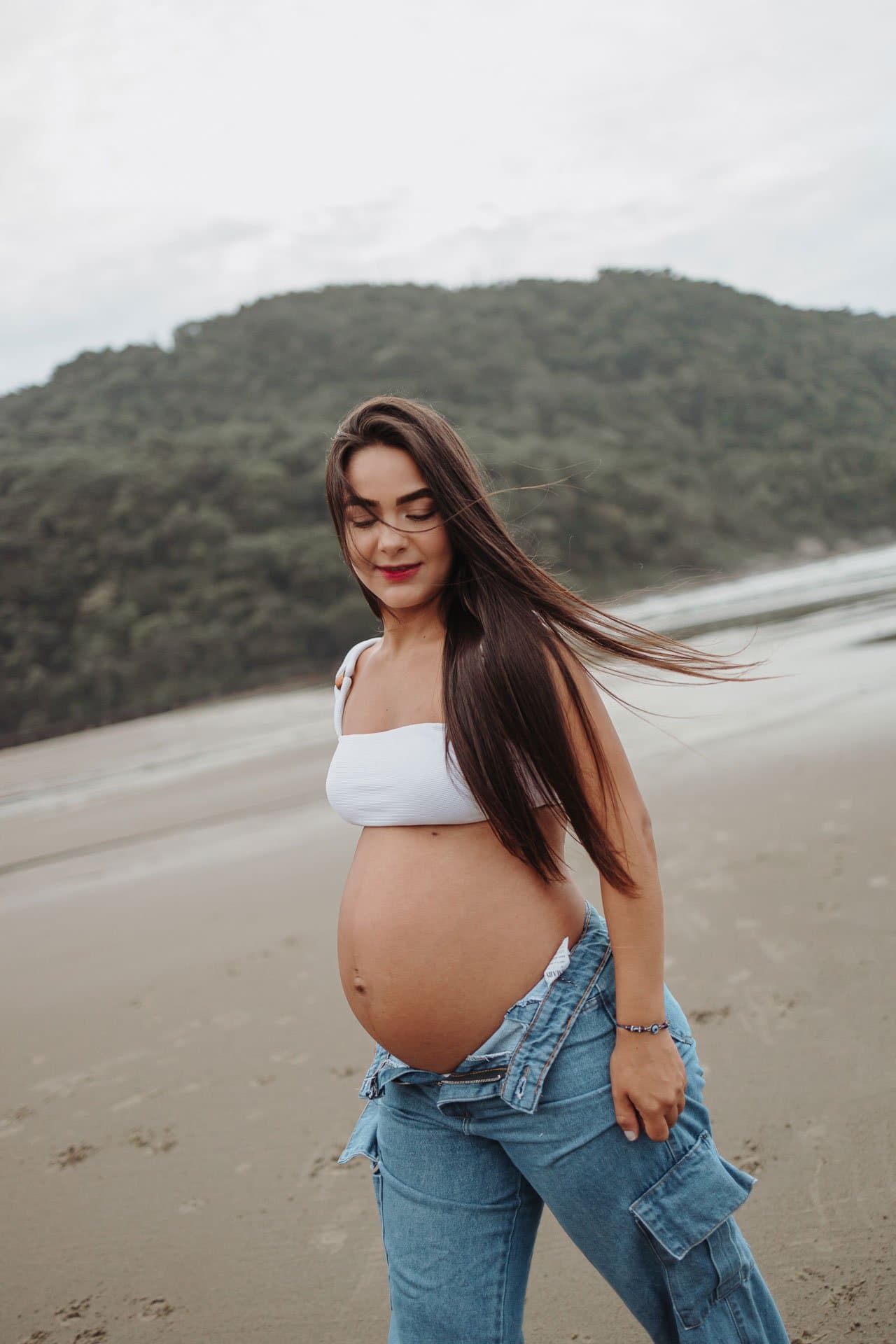 Gestante na praia com o vento no cabelo